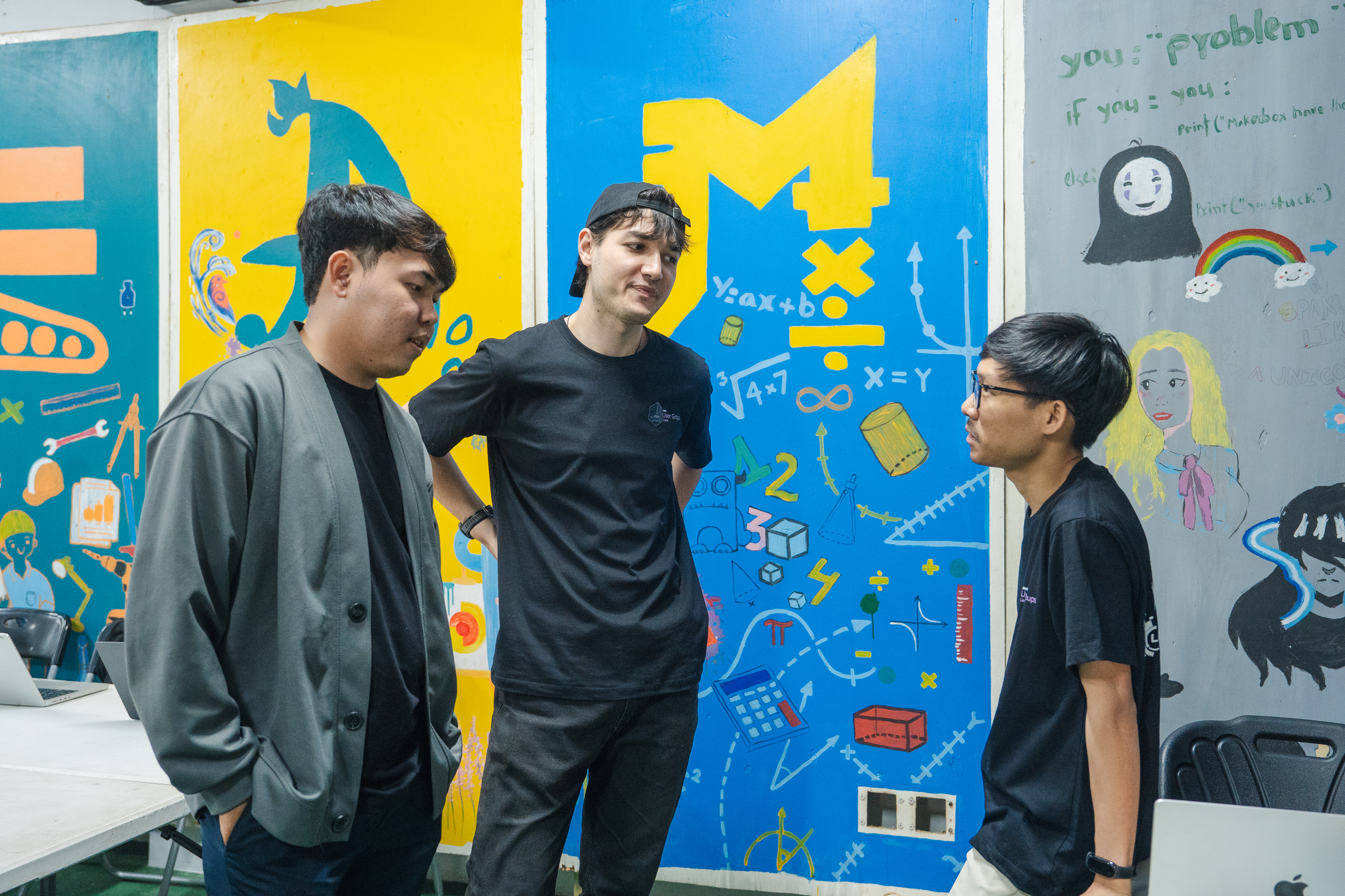 Ketsadaphone talking with two attendees in front of the colourful murals at MakerBox Lao
